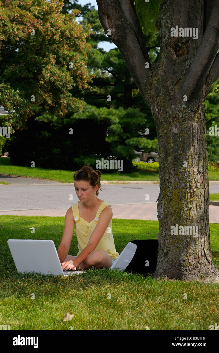 Niña haciendo los deberes en un portátil en el patio delantero bajo un árbol de arce Foto de stock
