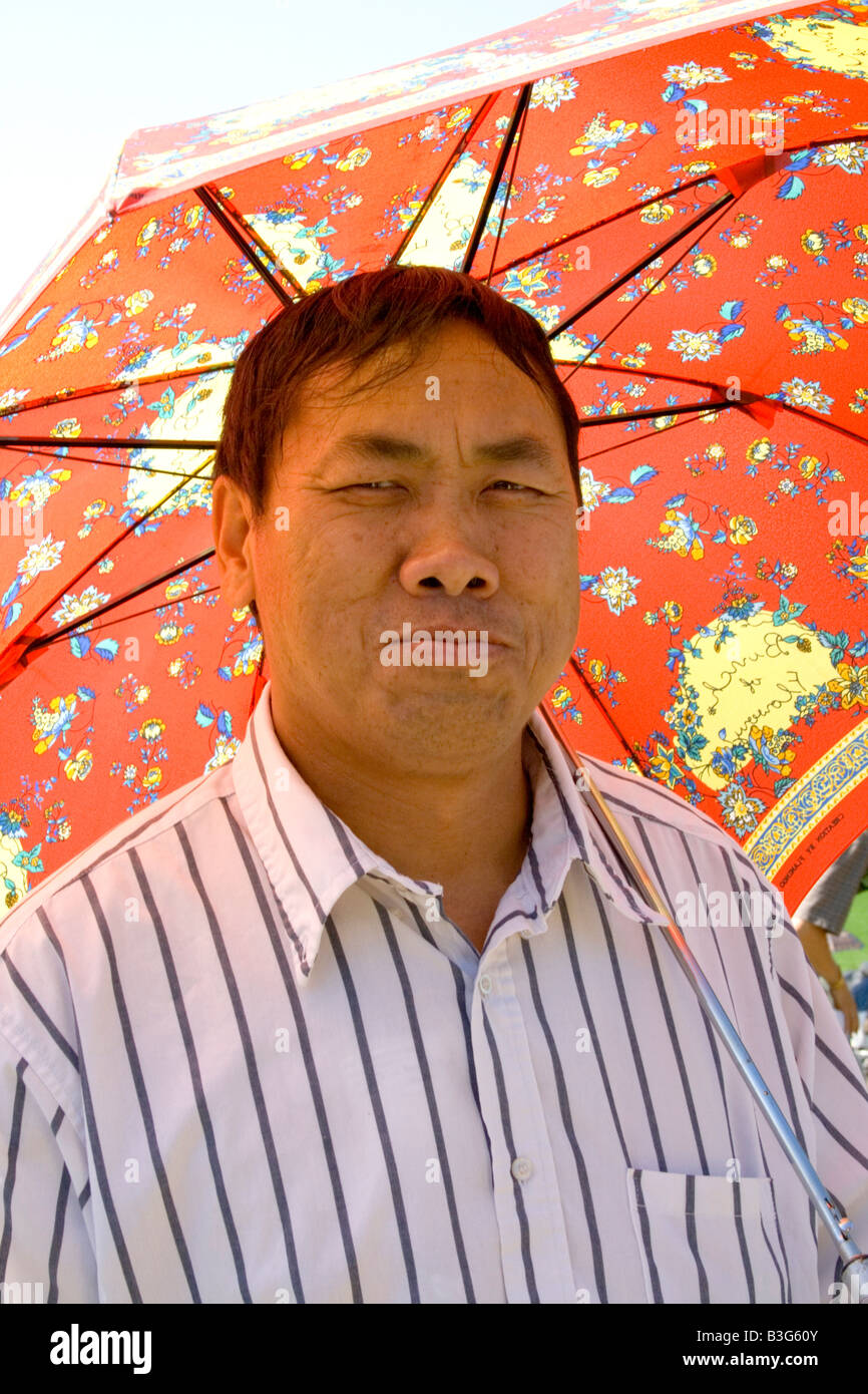 Apuesto hombre Hmong disfrutando de fiestas en multicolor sombrilla. Festival de Deportes de Hmong McMurray campo St Paul Minnesota, EE.UU. Foto de stock