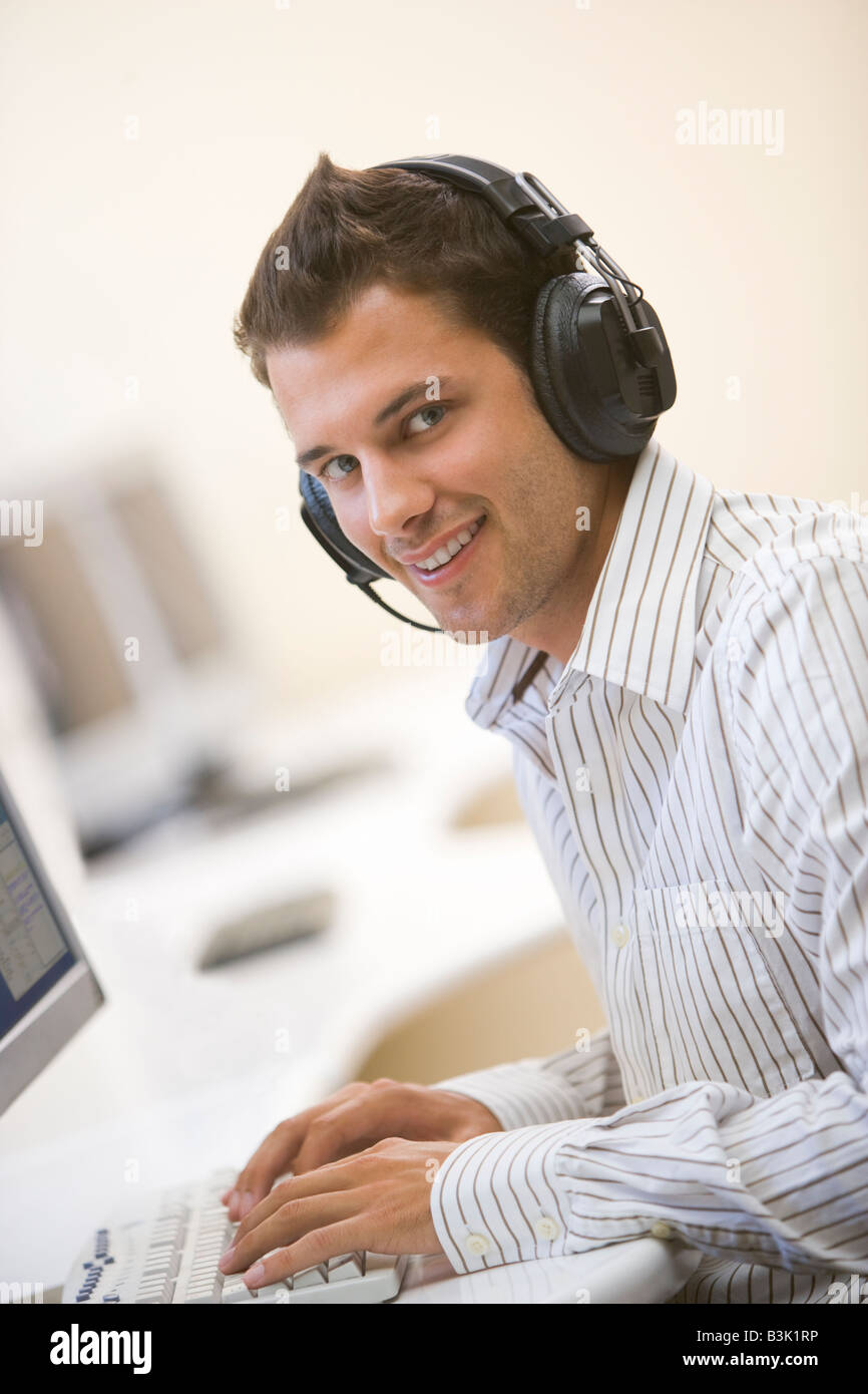 El hombre que lleva puestos los auriculares en el aula de informática  escribiendo y sonriente Fotografía de stock - Alamy