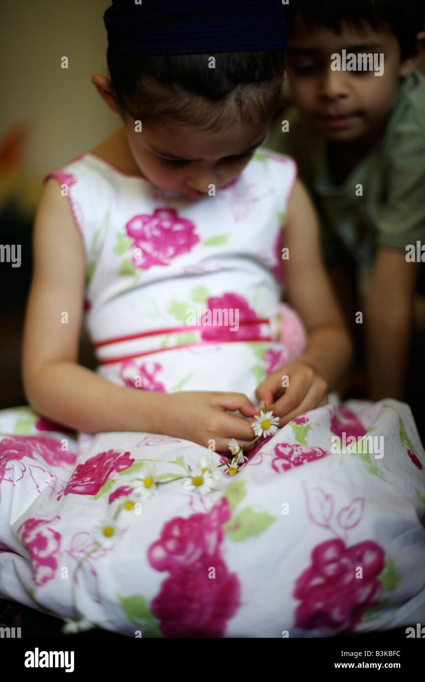 Cinco años de edad, niña hace daisy chain, wached por su hermano Foto de stock