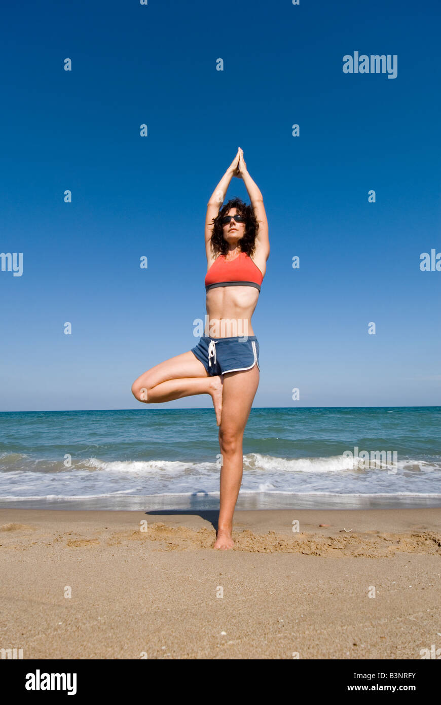 Publicado modelo fit joven haciendo ejercicios de estiramiento Estiramiento de yoga en una playa de arena Foto de stock