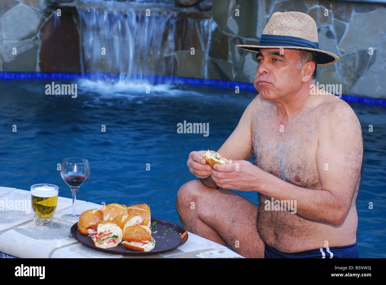 Hombre de Oriente Medio disfrutando de un sub bocadillo por una piscina en un resort Foto de stock