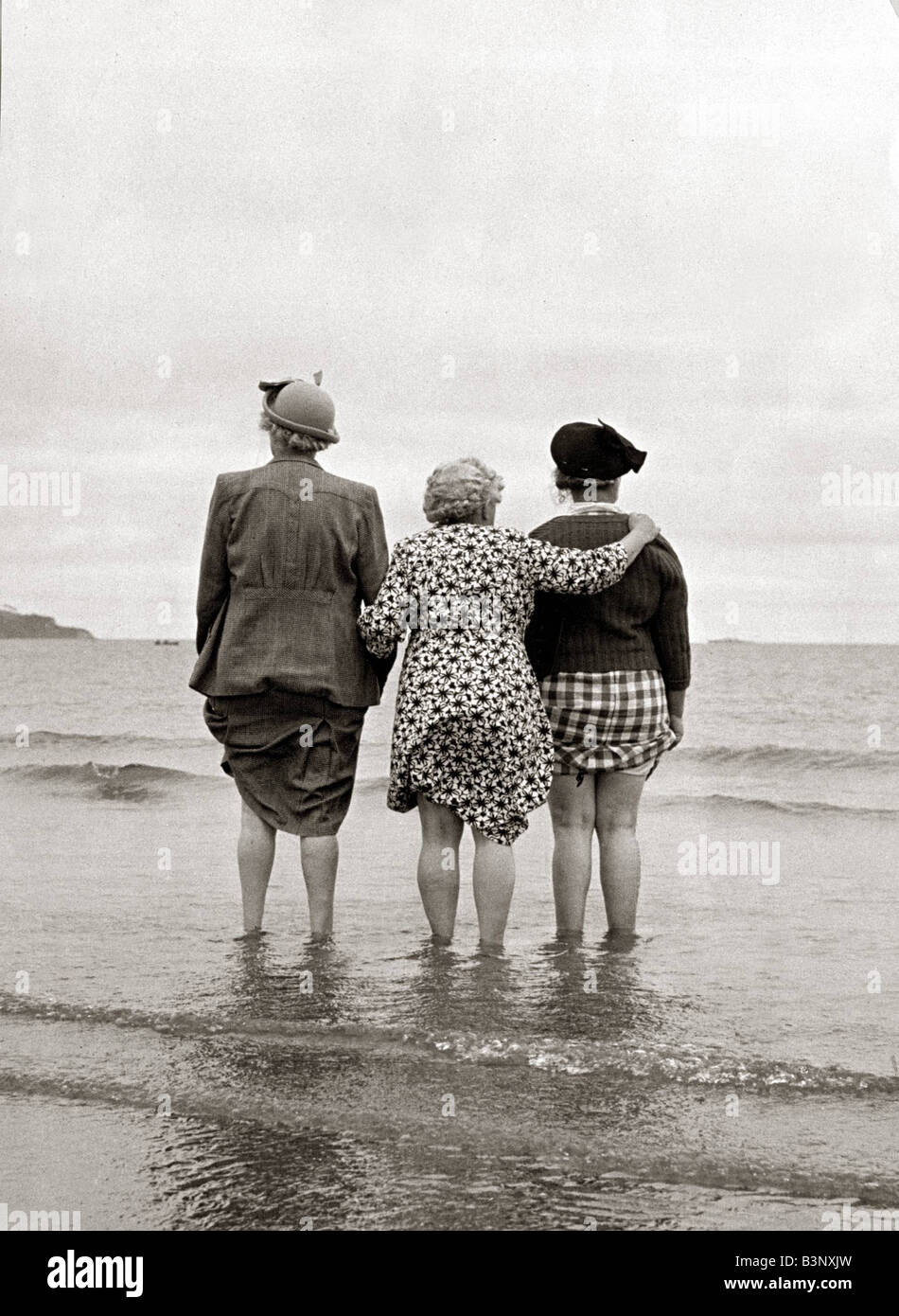 Tres mujeres que miran al mar, viendo barco desaparecer en el horizonte agarrando los dobladillos de sus vestidos de agosto de 1946 título Local relaxdimages Foto de stock