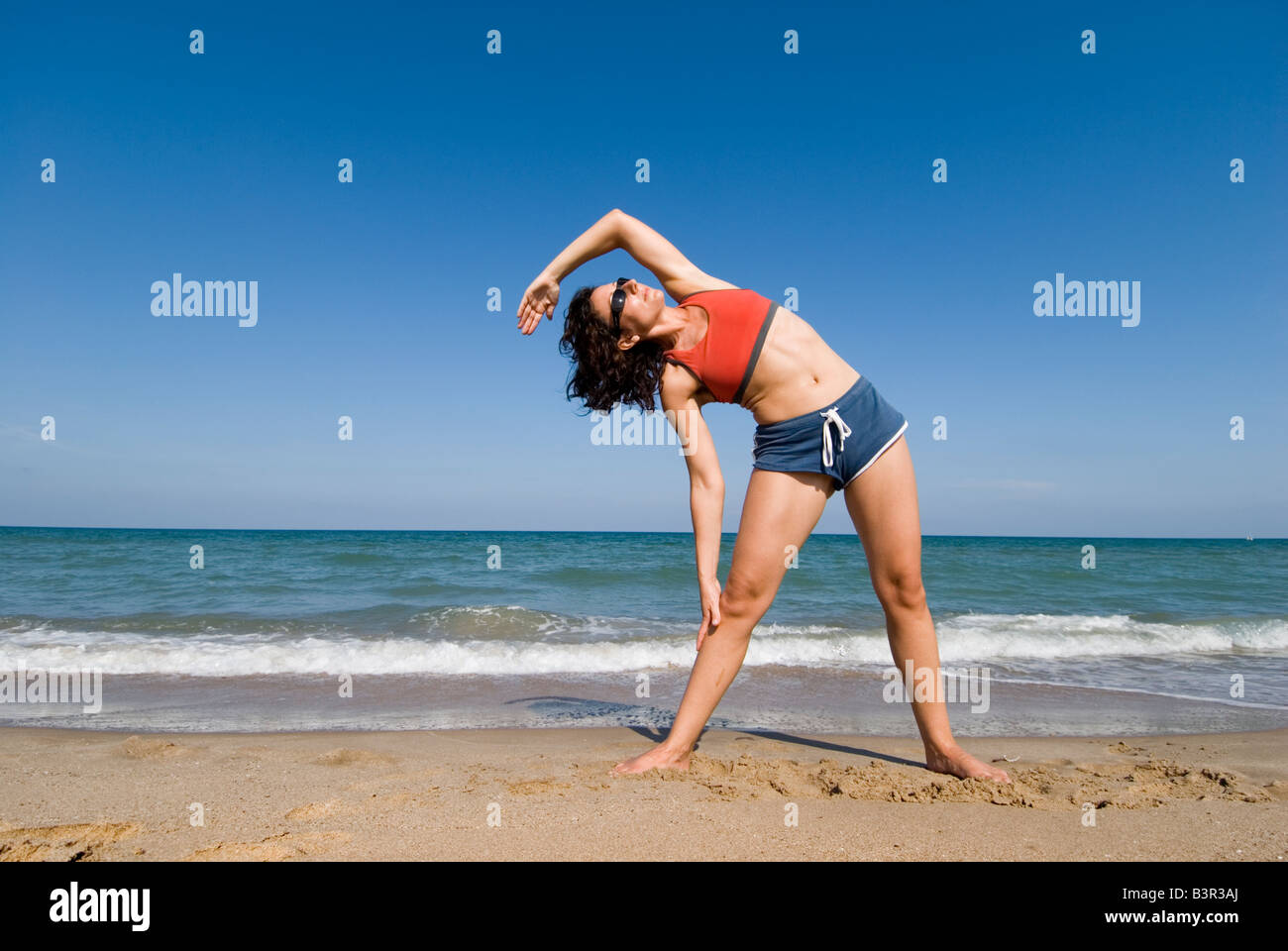 Publicado modelo fit joven haciendo ejercicios de estiramiento en una playa de arena Foto de stock