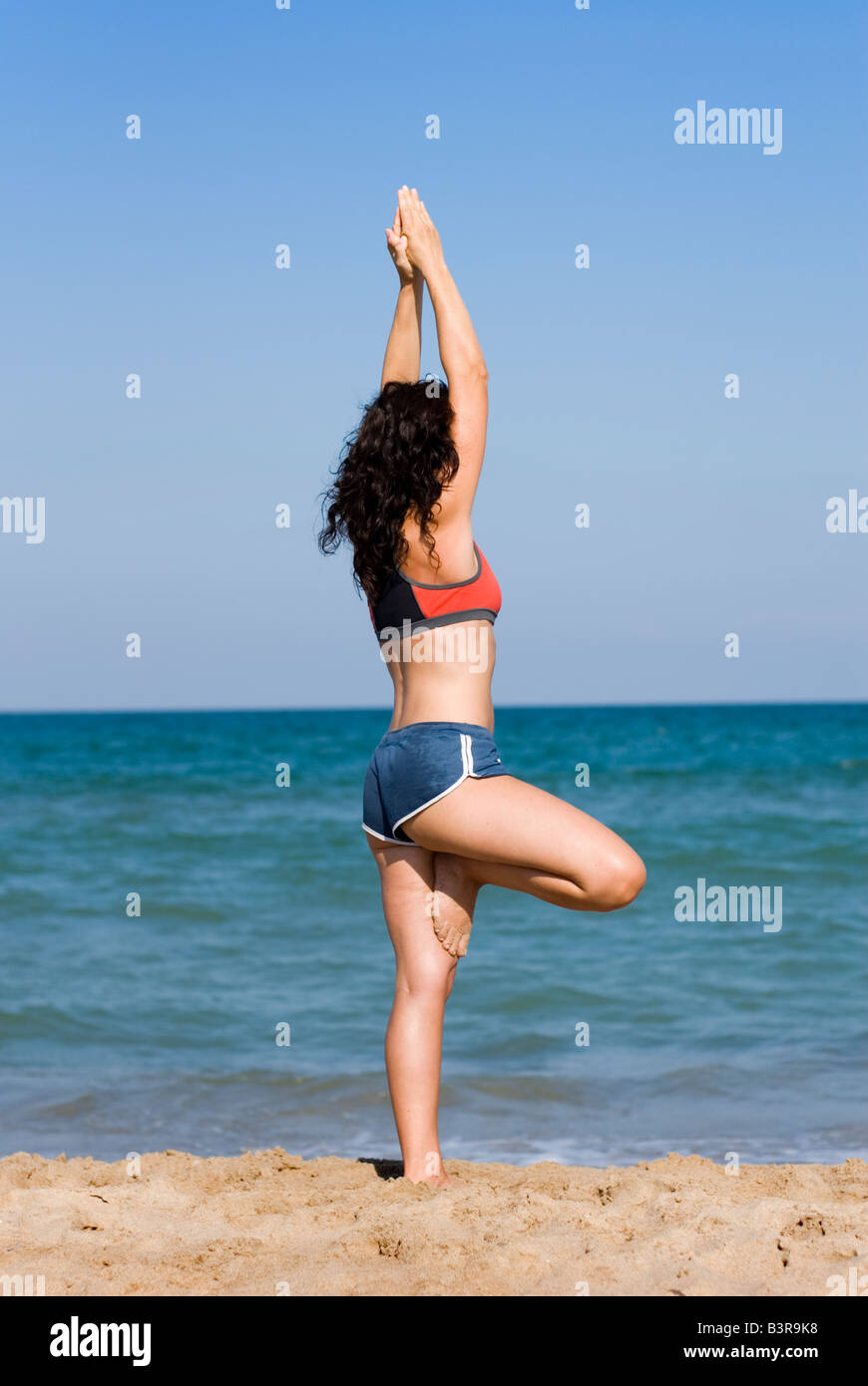 Publicado modelo fit joven haciendo ejercicios de estiramiento del yoga en una playa de arena Foto de stock