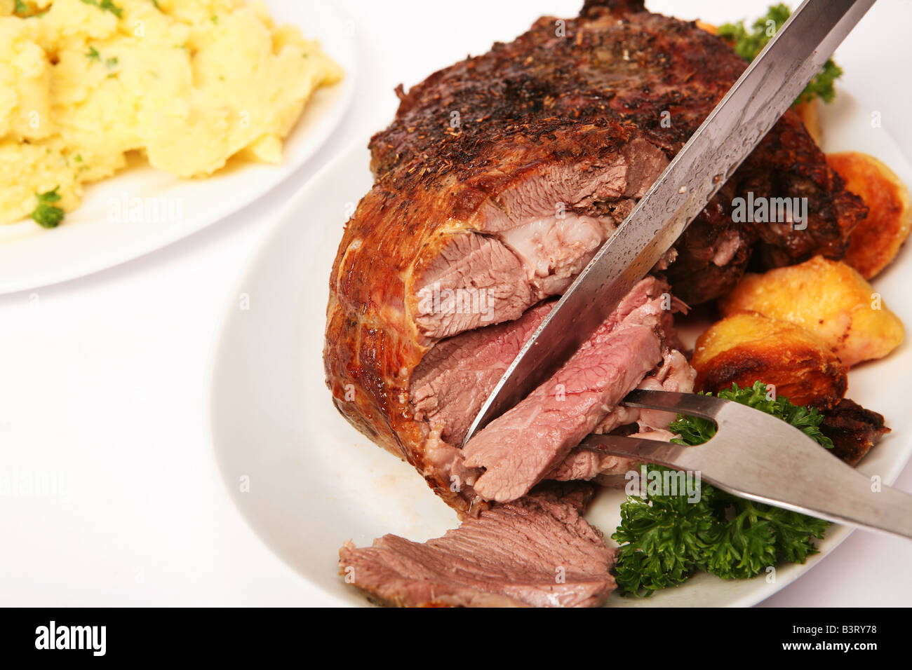 Una pierna de cordero deshuesada herbed están tallados con perejil y patatas  asadas en el plato y el puré de papas en el fondo Fotografía de stock -  Alamy