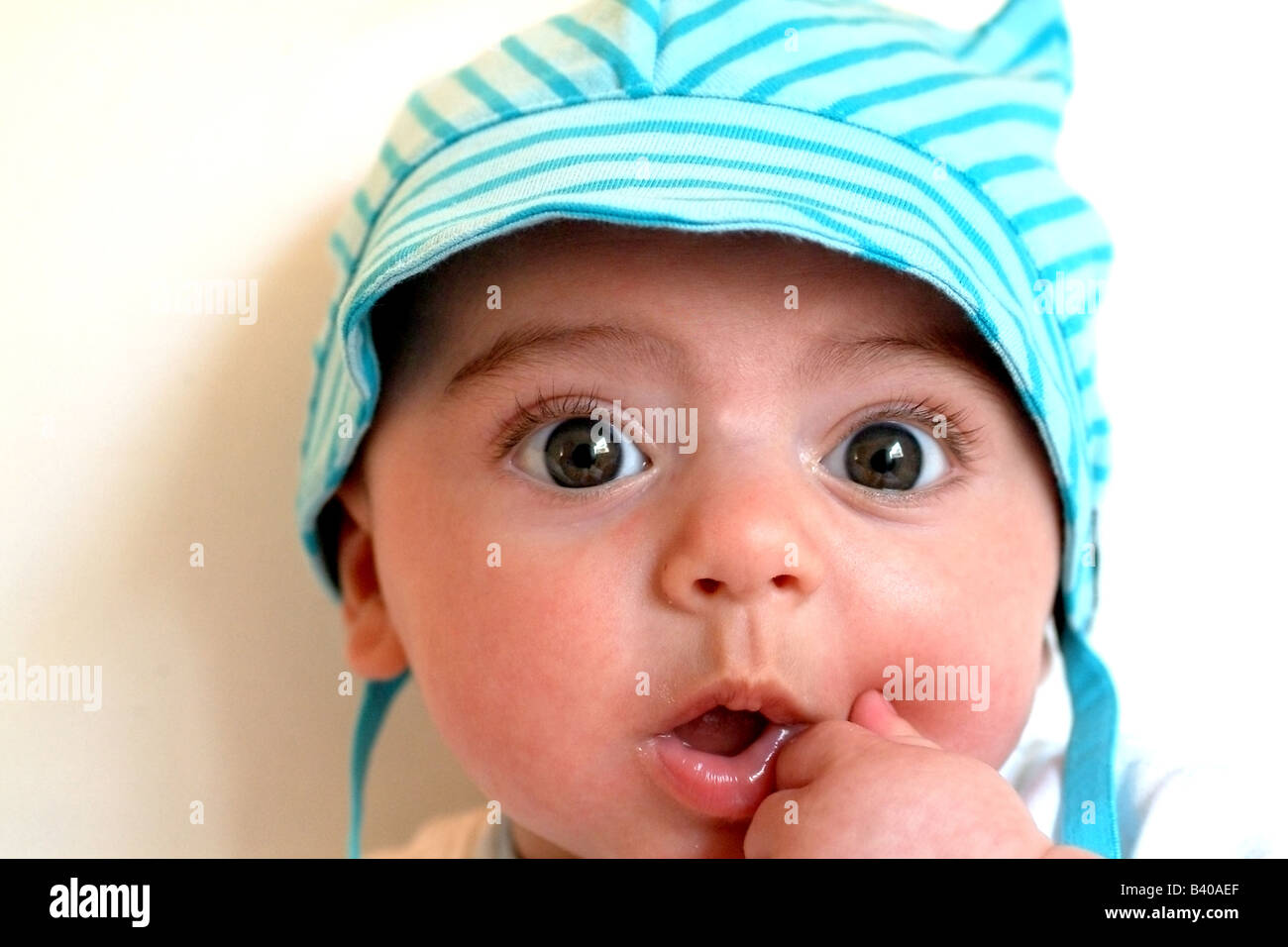 Cute Baby Boy vistiendo un sombrero de rayas creemos azul y mirando sorprendido Foto de stock
