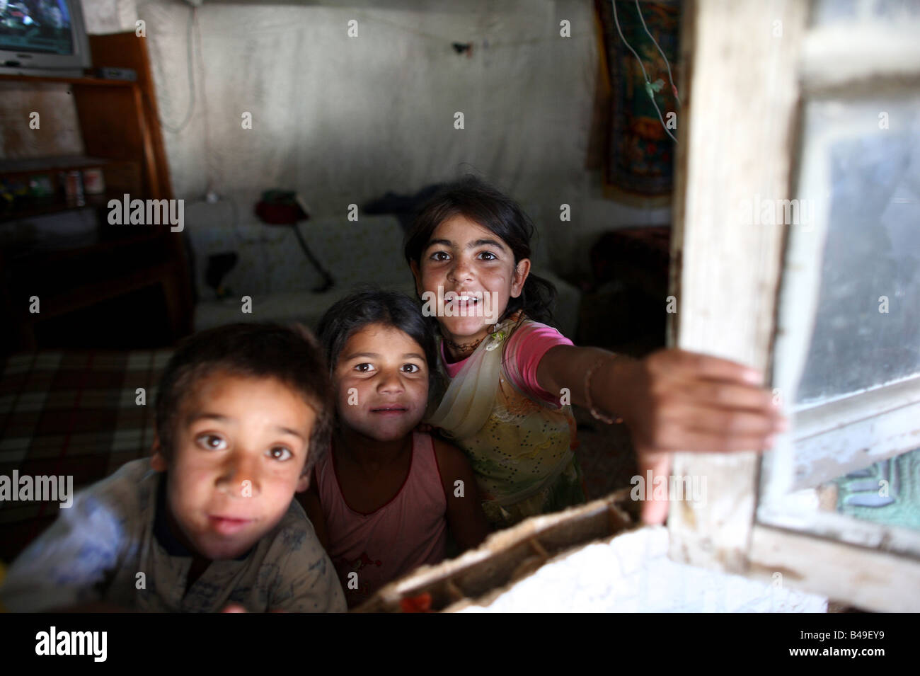 Los niños gitanos romaníes mirando a través de una ventana en su casa en compartir, un tugurio junto a un vertedero de basura en las afueras de Tirana, Albania Foto de stock