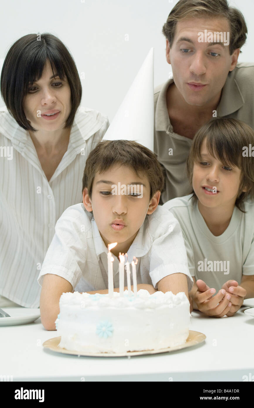 Familia viendo boy soplar las velas en el pastel de cumpleaños Foto de stock