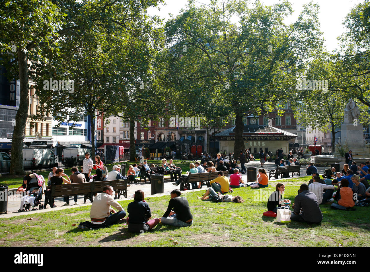 Los turistas y estudiantes disfrutar del sol relajándose en pasto en Leicester Square London West End Entertainment District teatro UK Foto de stock