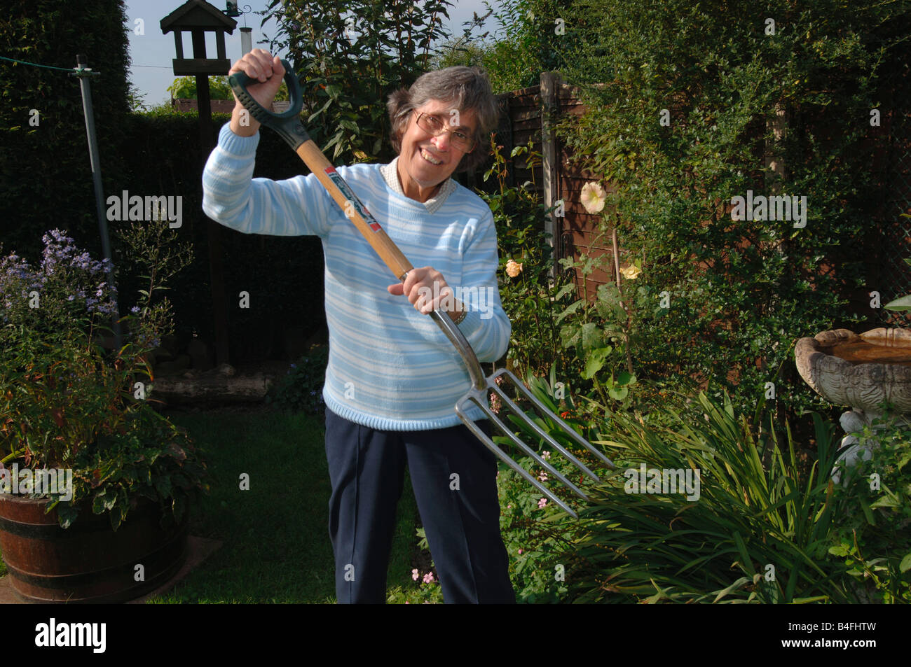 Una mujer de más de setenta posando con una horquilla de jardín Foto de stock