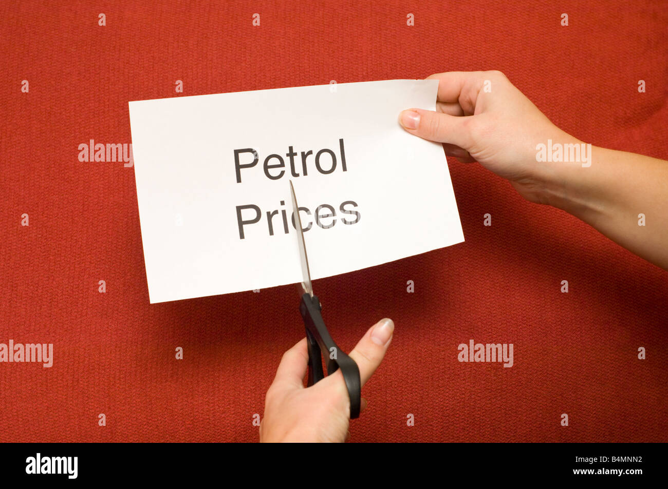 Imagen de persona cortando un trozo de papel con "los precios de la gasolina" escrito en él con un par de tijeras Foto de stock