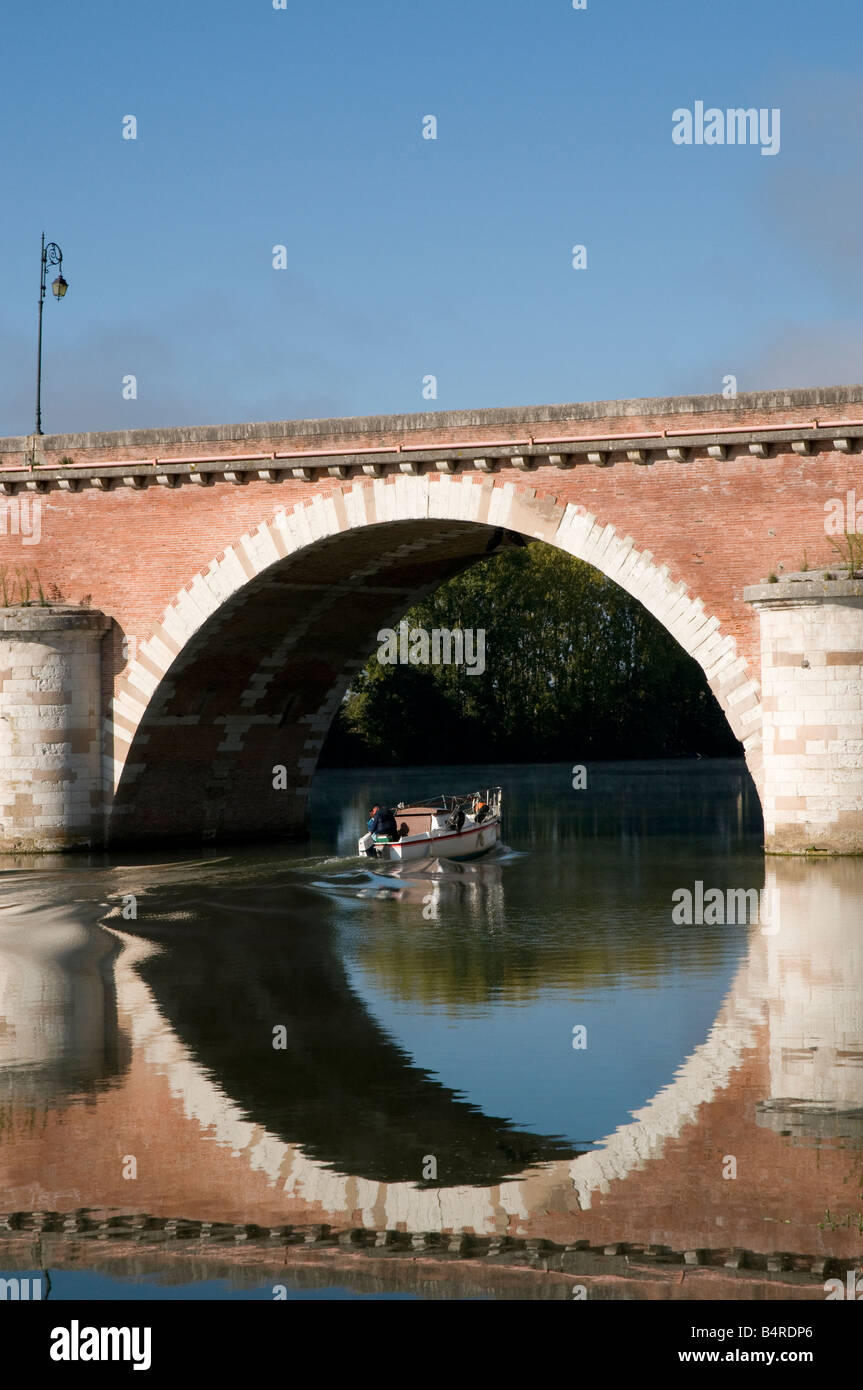 Francia. Circular perfecto reflejo en el agua del barco navega bajo el arco en el puente sobre el río Tarn en Moissac Foto de stock