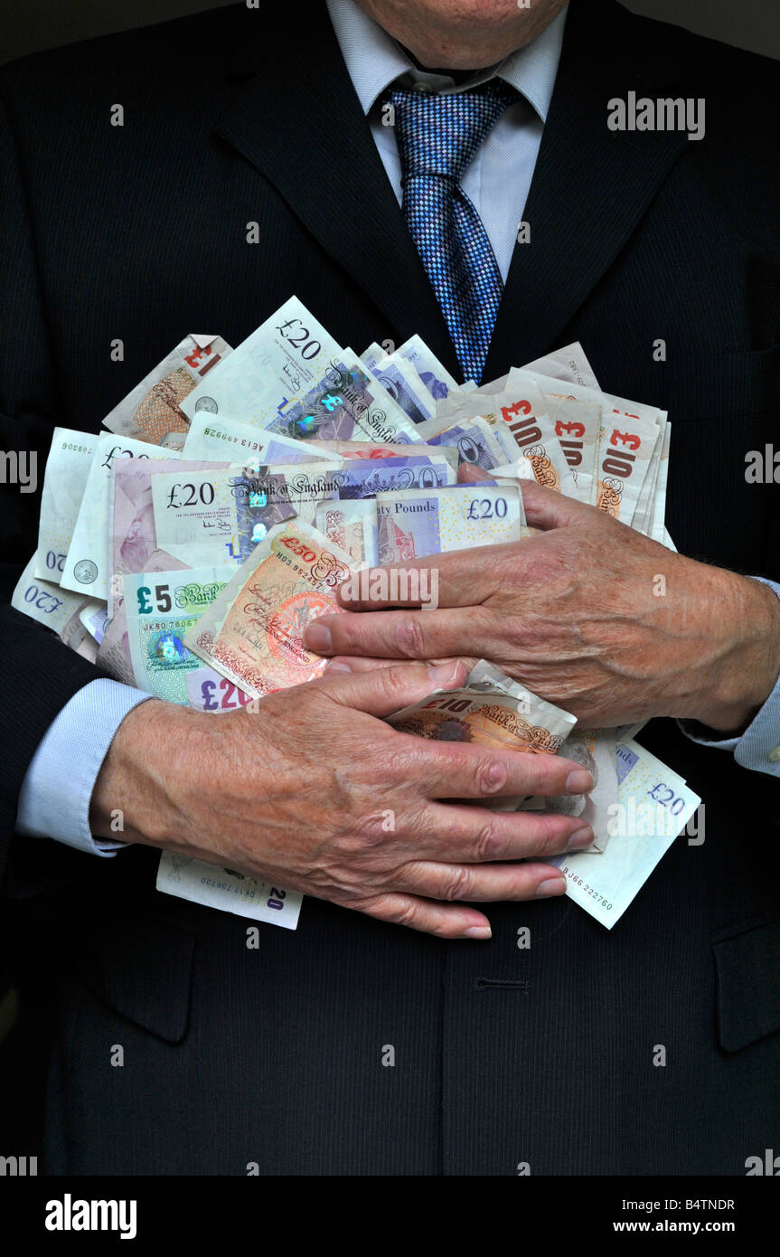 Hombre que lleva la oficina traje de negocios manos agarrando pila Reino Unido libra dinero en efectivo en moneda el banco señala un concepto de dinero para los banqueros grasa gato avaricia por los hombres en trajes Foto de stock