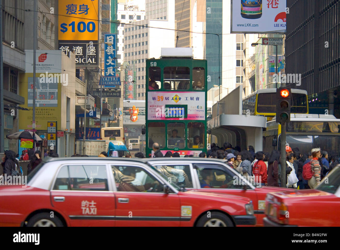 Una tradicional antiguo tranvía viajando a través de la zona de Wan Chai en la isla de Hong Kong con el taxi rojo familiar en primer plano. Foto de stock