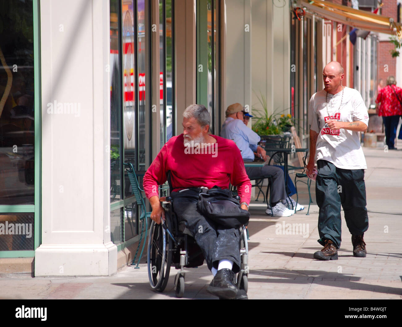 Hombre en una silla de ruedas en una acera de la ciudad Foto de stock