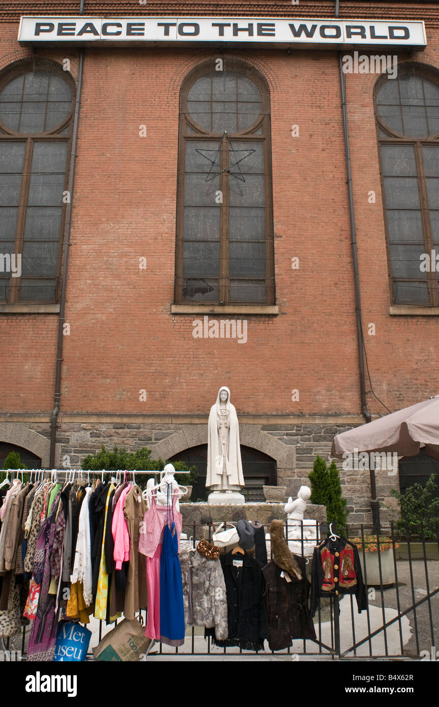 La paz en el mundo signo en NYC iglesia Virgen María estatua acera mercadillo venta ropa sobre la valla Foto de stock