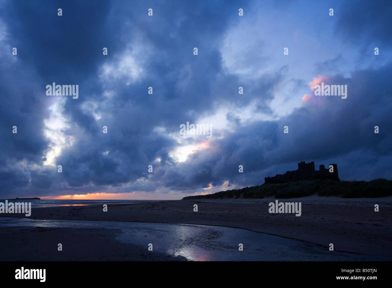 Temprano en la mañana la vista de Bamburgh Castle Northumberland tomada desde la playa con stream en primer plano Foto de stock