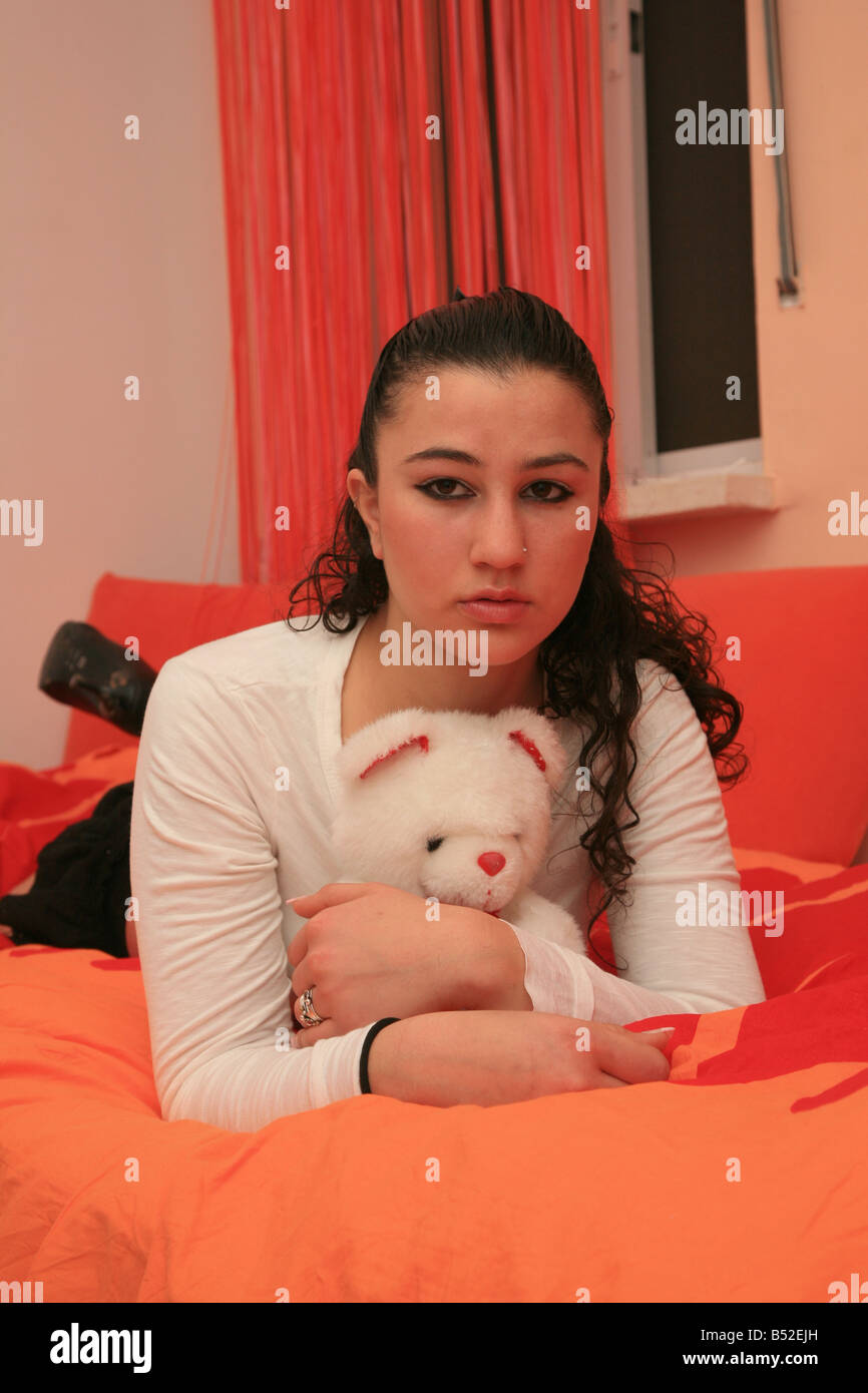 Adolescente con un make up acostada en la cama, sosteniendo un oso de peluche, UK 2008 Foto de stock
