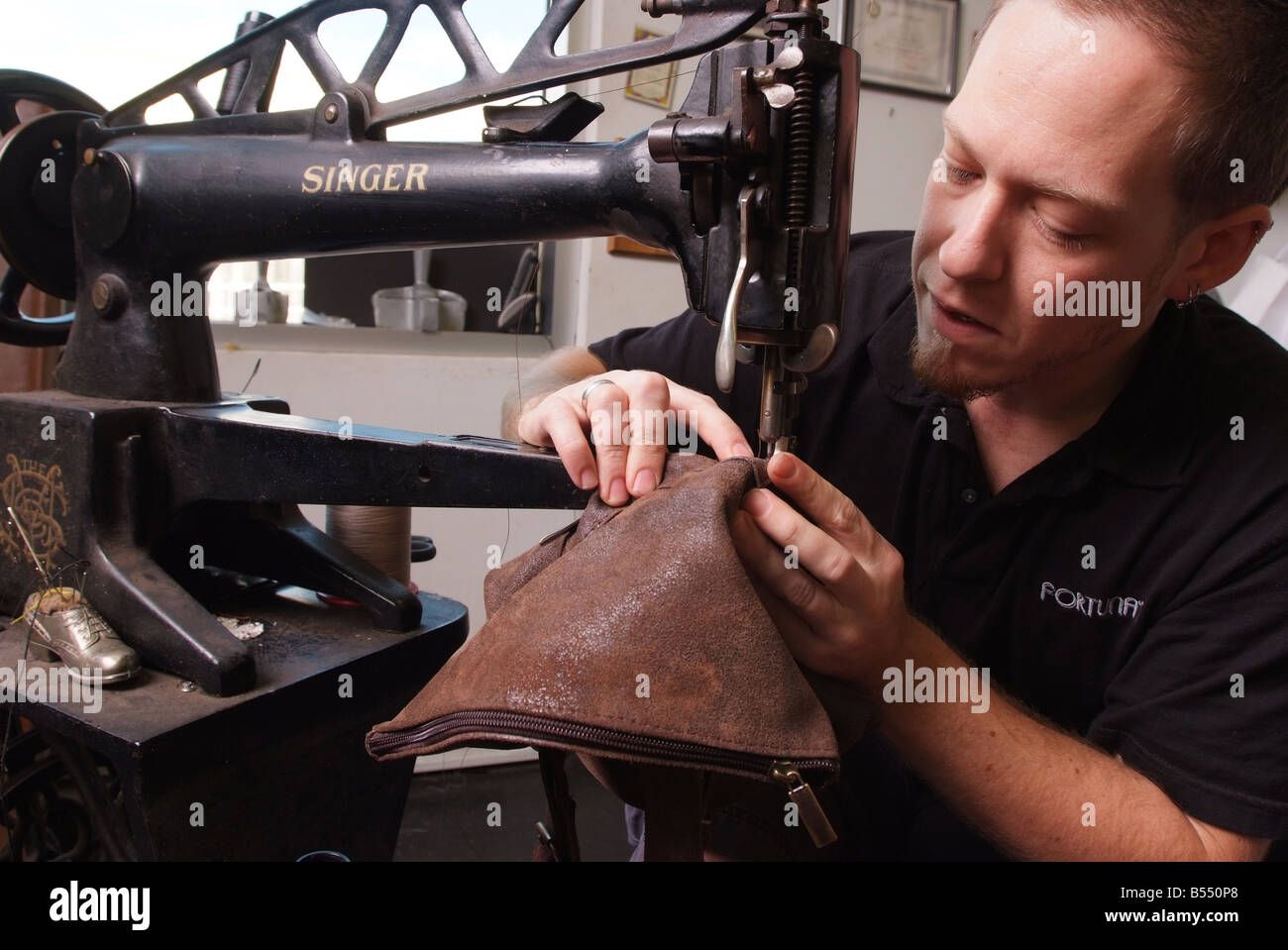 Un hombre utiliza una antigua máquina de coser Singer para la reparación de artículos de cuero en una pequeña tienda en Maryland, EE.UU. Foto de stock