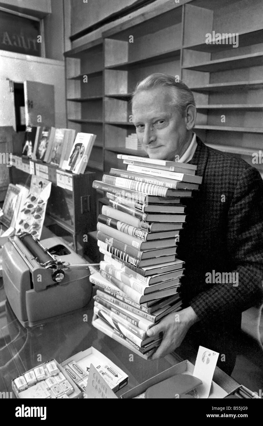 Tendero Leslie Davies en el mostrador de su tienda de tabaco y dulces en Deganwy, con su máquina de escribir y unos pocos de los libros que ha escrito entre vender lollipops y cigarrillos. Diciembre de 1969 Z12344-002 Foto de stock