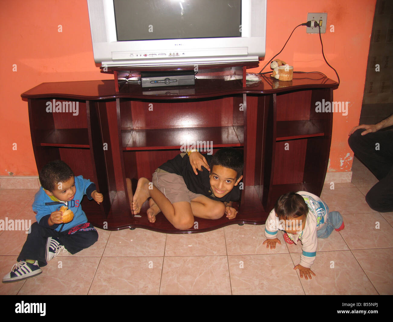Tres primos feliz (Felipe, Samuel, Gabriel), uno de ellos dentro de un rack de TV, de Sepetiba, Río de Janeiro, Brasil / Brazil Foto de stock