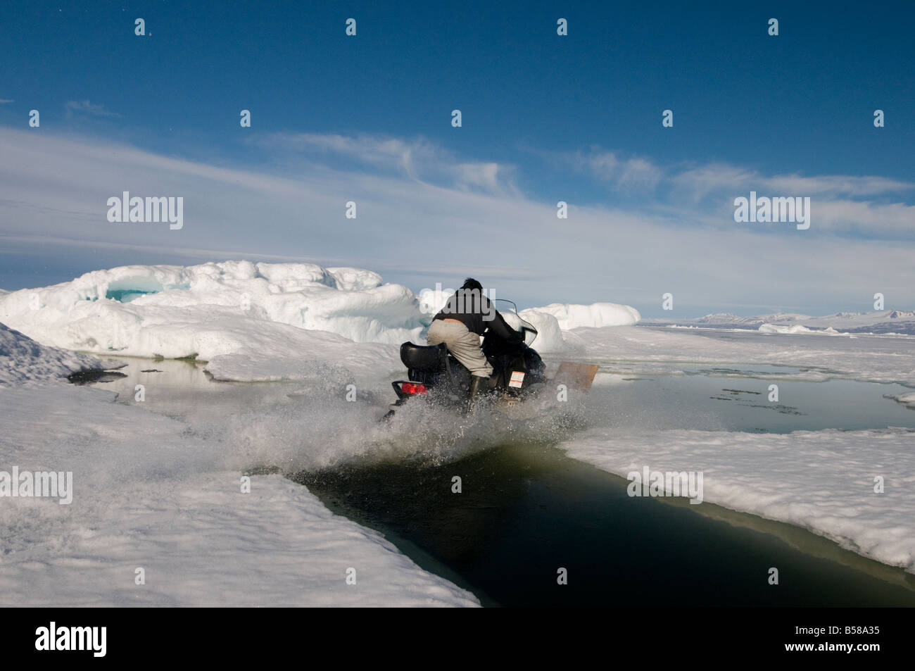 Cruzando peligrosamente amplia primavera grietas en el océano Ártico por conducir la moto de nieve a través de la superficie del agua Foto de stock