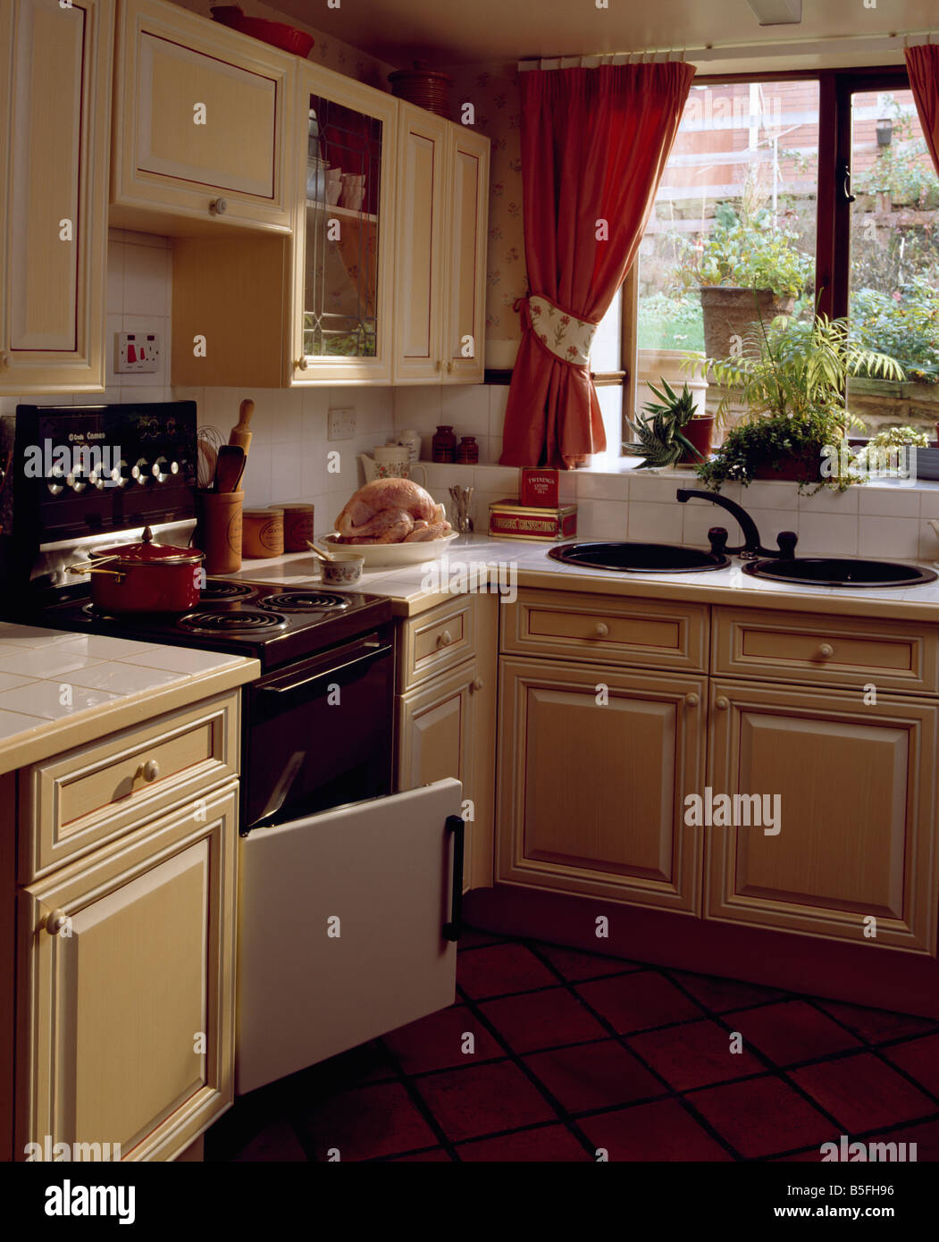 Circular doble se hunde debajo de la ventana con cortinas rojas en la  pequeña cocina equipada con horno la puerta abierta Fotografía de stock -  Alamy