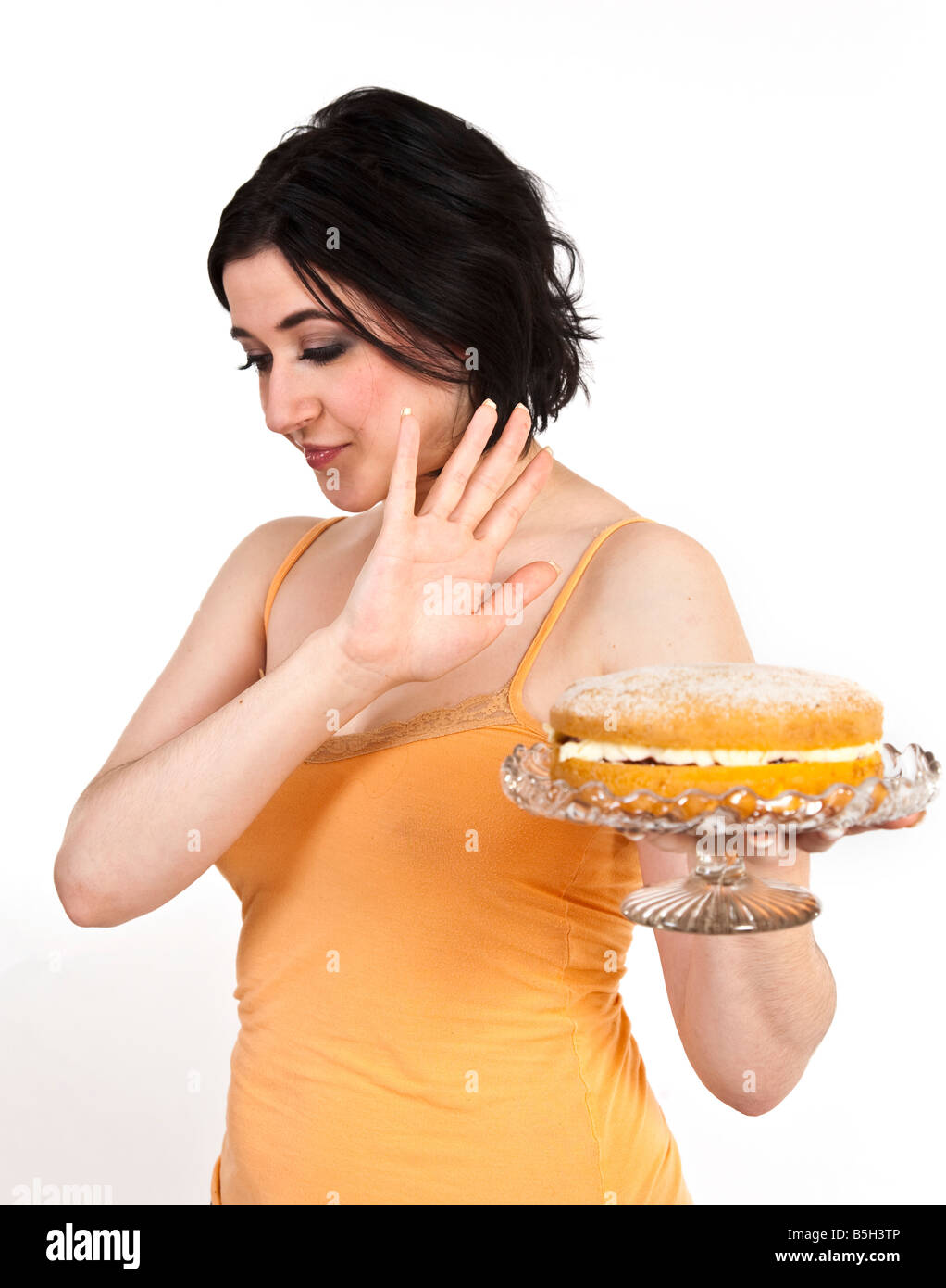 Una joven mujer intenta resistir la tentación de una tarta de crema. Foto de stock