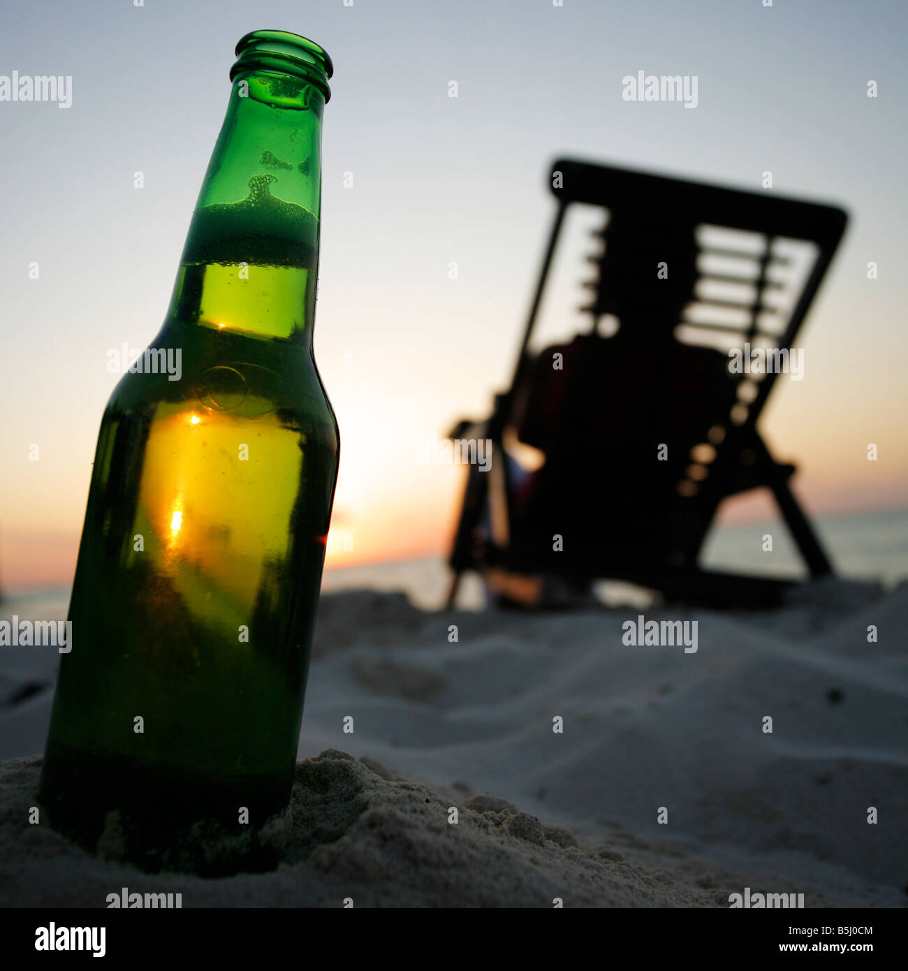 Sunset con cerveza bopttle y una mujer en una tumbona. Foto de stock
