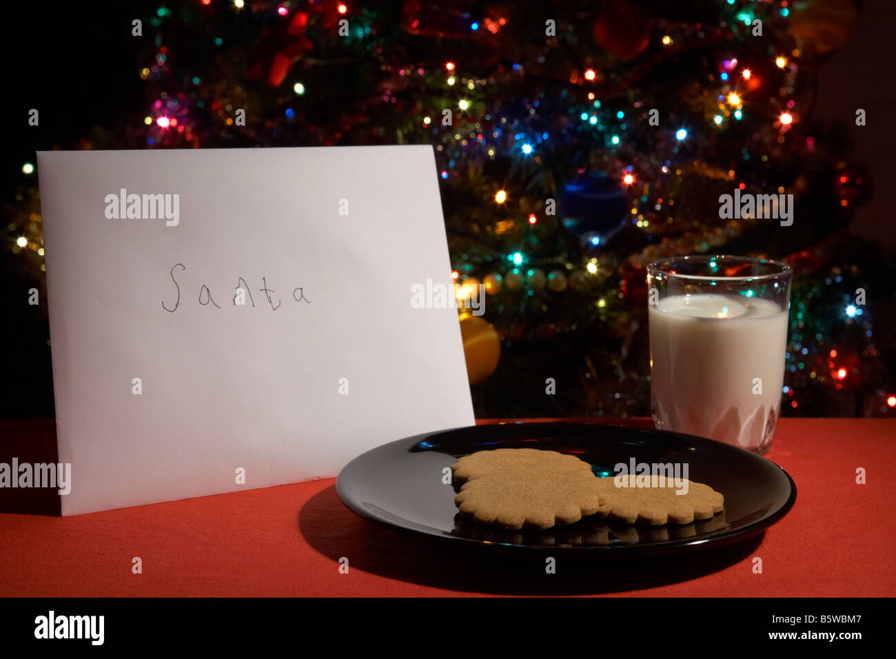 Childs carta a santa quedaron en la víspera de Navidad con galletas y un vaso de leche delante del árbol de navidad Foto de stock