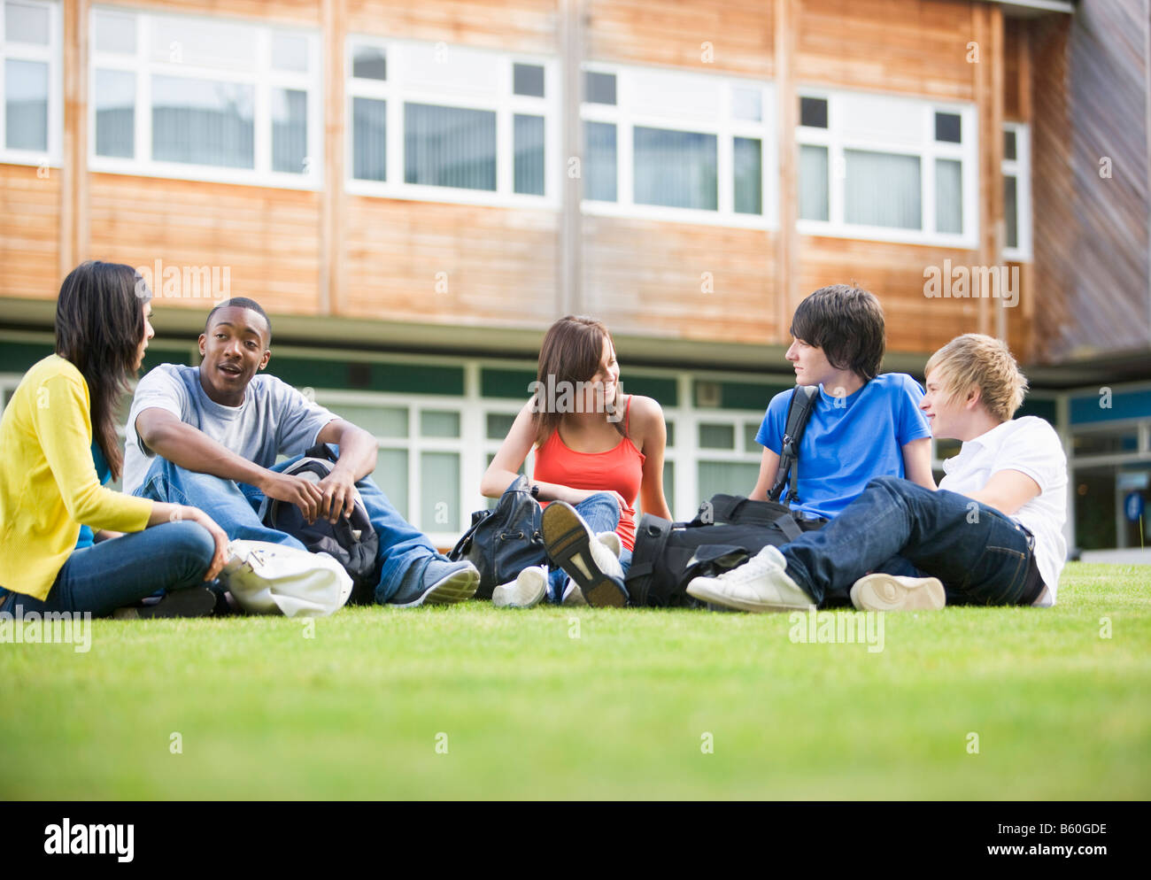Cinco estudiantes sentados al aire libre en el césped hablando Foto de stock