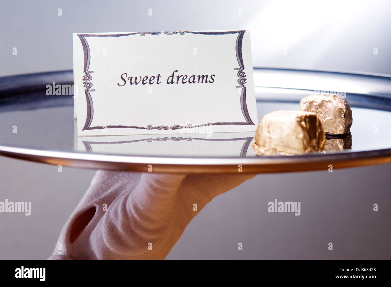 Close-up de la mano de un camarero llevando un plato con dulces sueños nota y chocolates Foto de stock