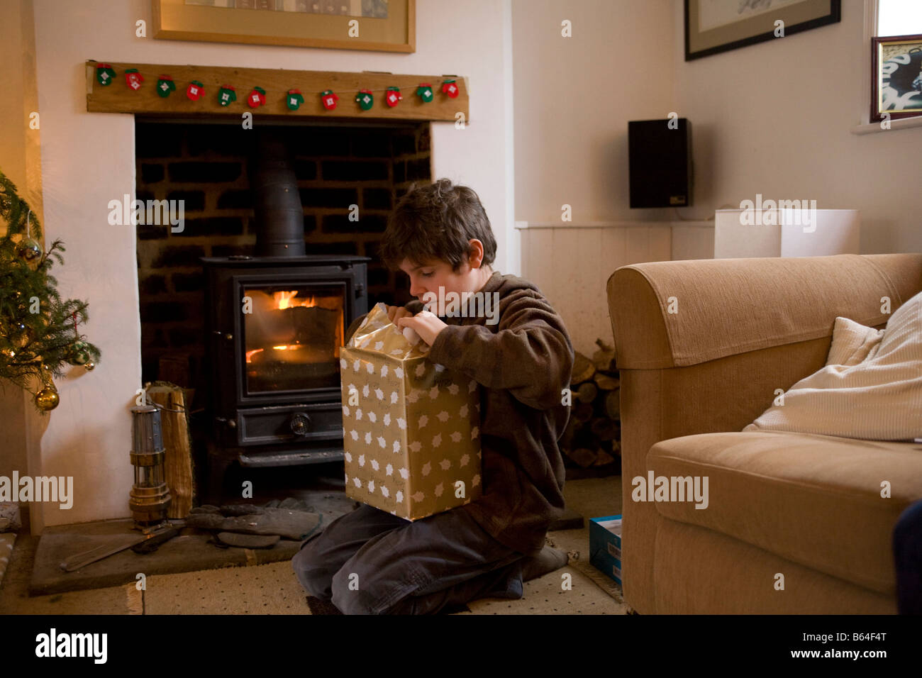 Muchacho de 11 años abrir un regalo de navidad enfrente de un incendio real Foto de stock
