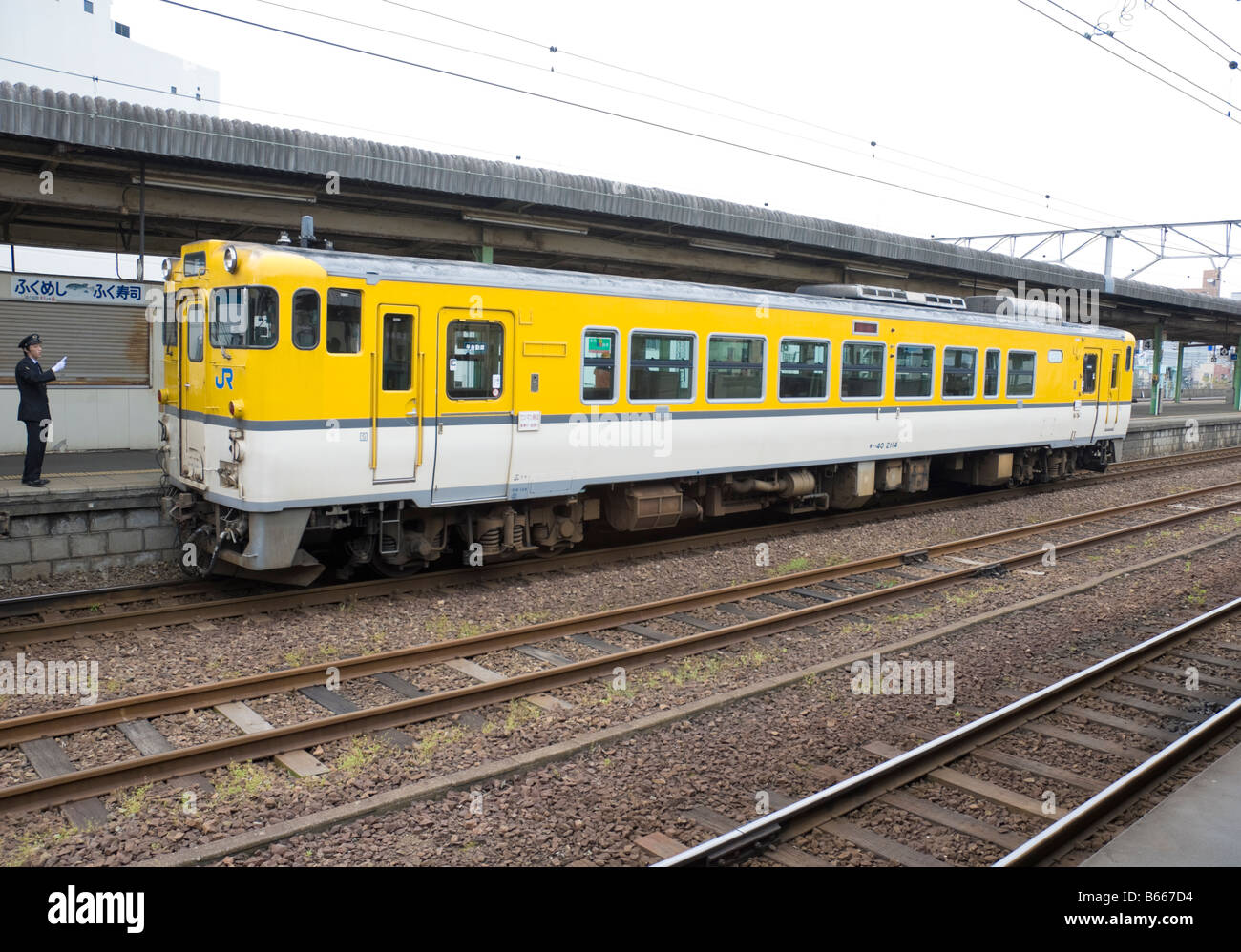 El guardia ve fuera de un color amarillo brillante único carro de tren diesel. Los trenes como este son comunes en japonés rural líneas de ferrocarril. Foto de stock