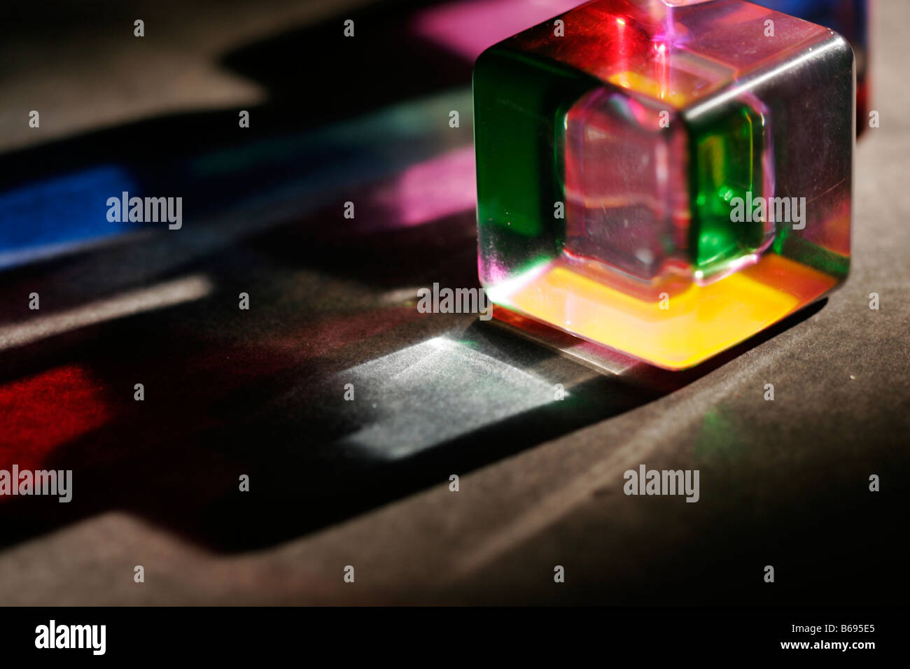 Cubo acrílico de color con luz brillando con colores derramados desde el prisma a la mesa Foto de stock
