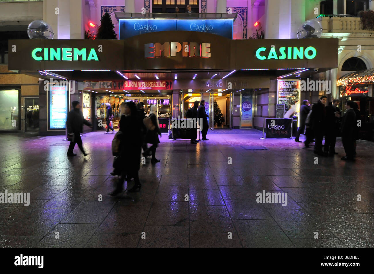 Personas en el pavimento fuera de Empire Leicester Square cine casino locales de entretenimiento cerise coloreado iluminación de inundación Londres, Inglaterra, Reino Unido Foto de stock