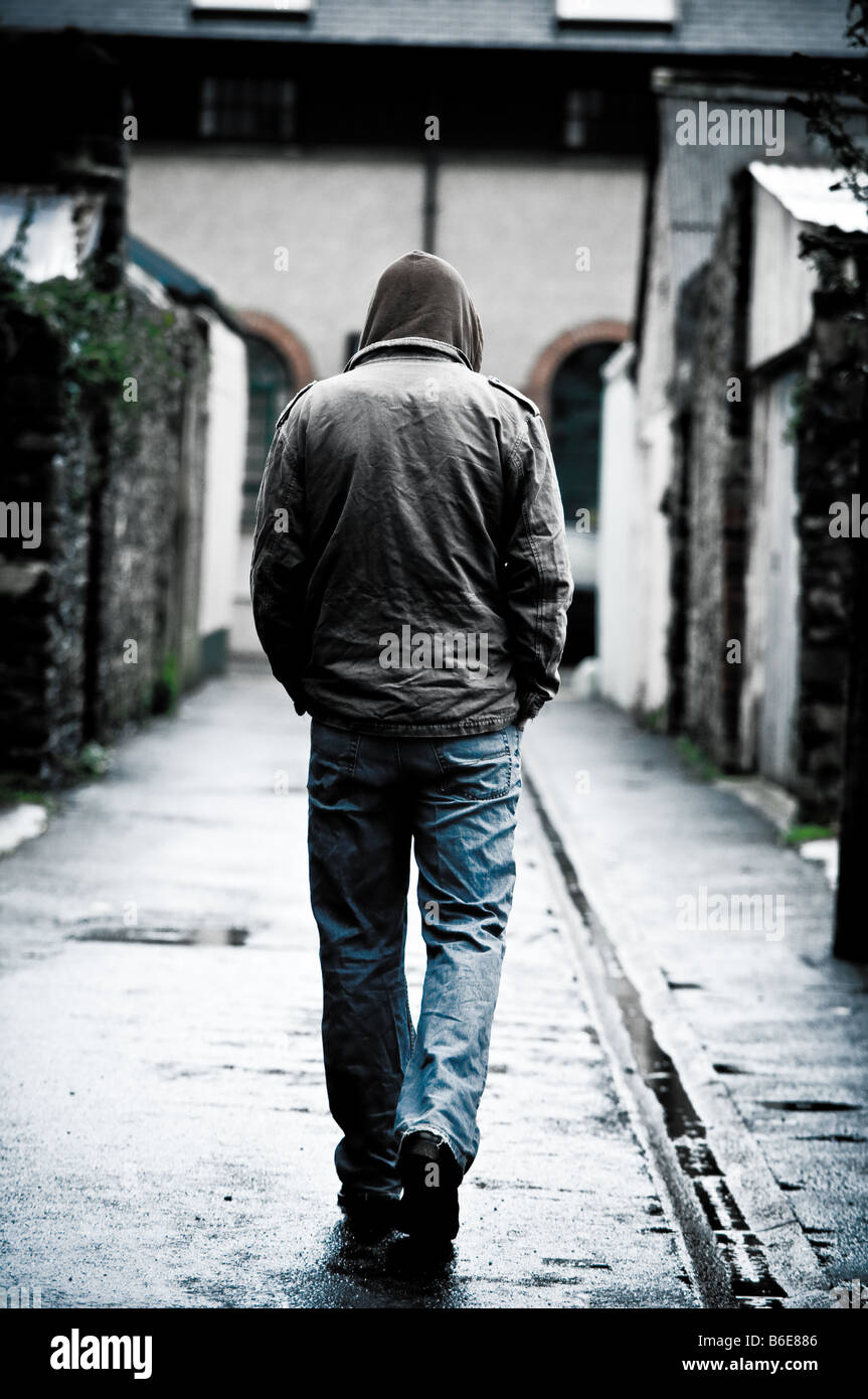 Joven llevaba una chaqueta con capucha solos y aislados, caminando por un callejón en una ciudad UK visto desde atrás caminando Foto de stock