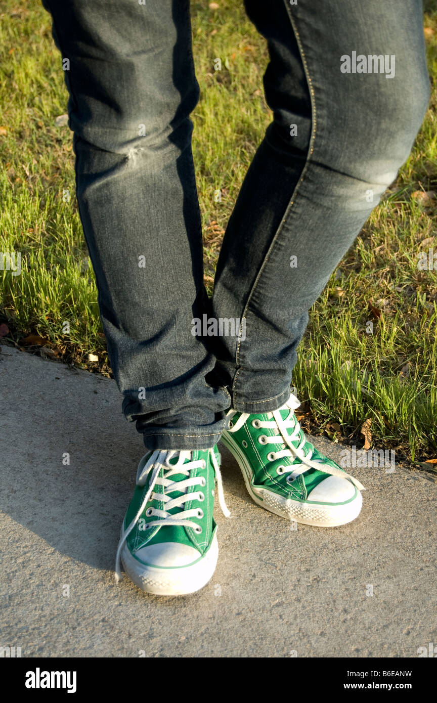 Un adolescente piernas vistiendo skinny jeans denim azul y verde Converse  zapatillas sobre sus pies Fotografía de stock - Alamy