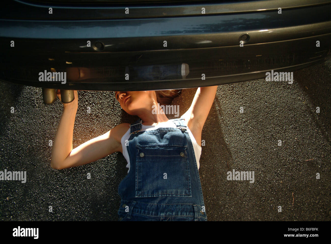 Joven en ropa de trabajo está tumbado bajo su coche mientras arreglando Foto de stock