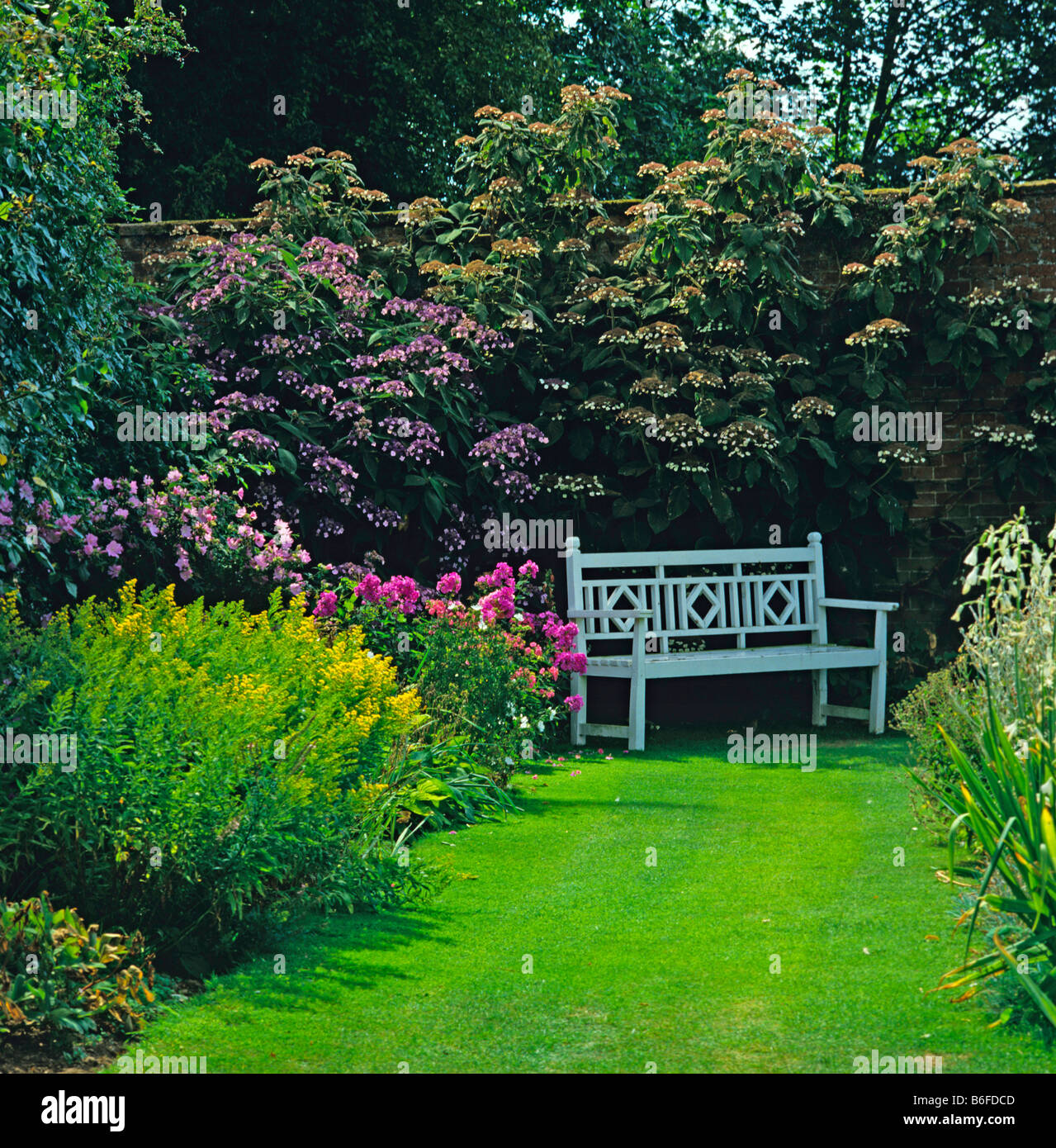 Asiento en el romántico jardín amurallado con una colorida flor fronteras Foto de stock