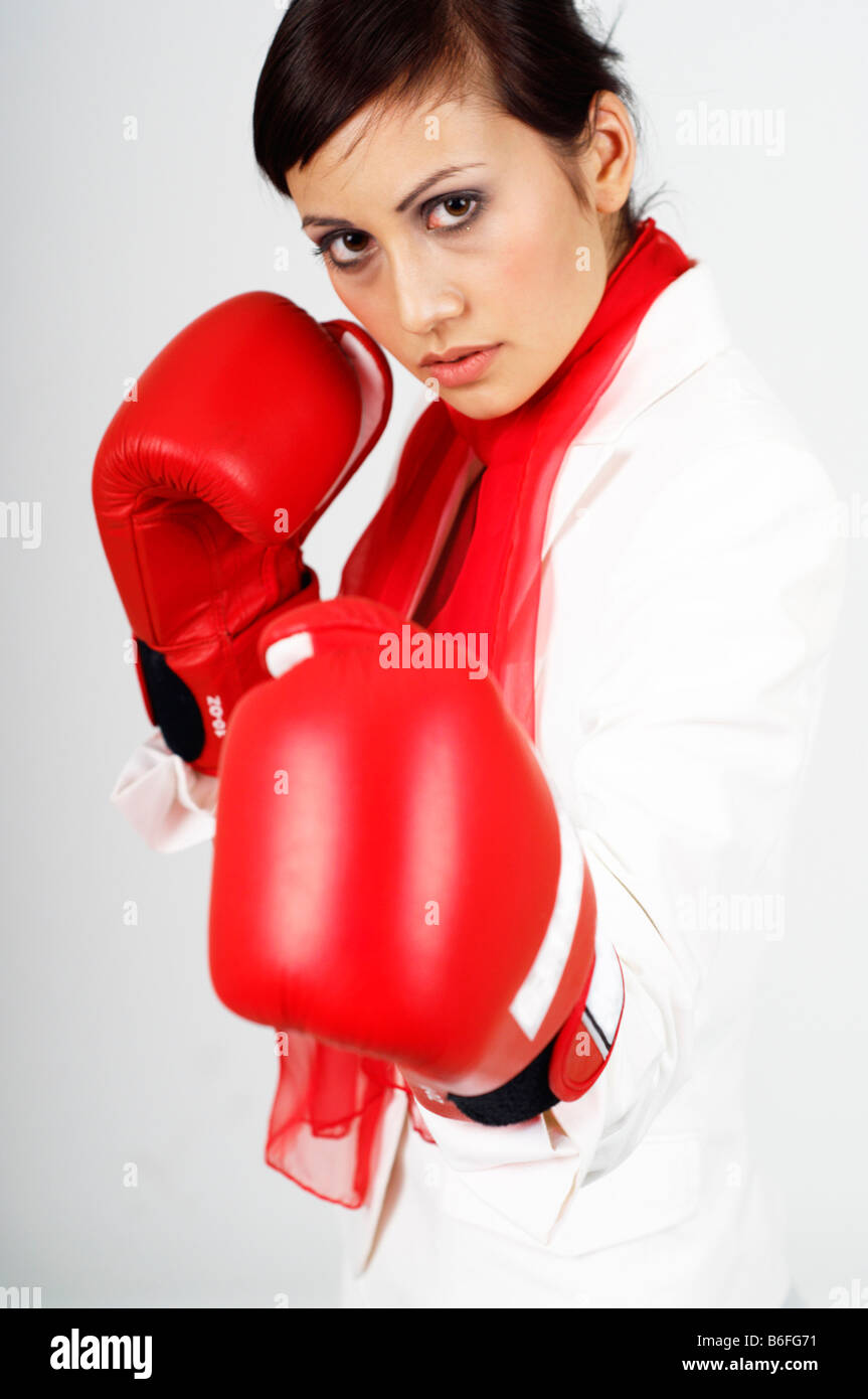 Profesional joven mujer de negocios usando guantes de boxeo se sitúa en una actitud agresiva Foto de stock