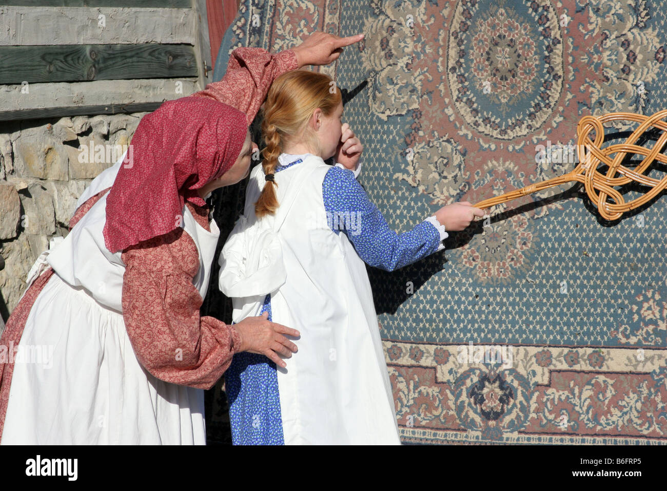 Una madre que muestra a una niña cómo vencer a una alfombra en el estilo de vida del viejo oeste y forma y la chica sujetando la nariz Foto de stock