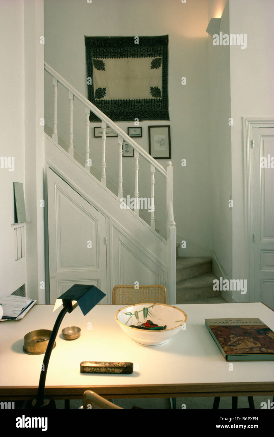 Lámpara moderna negro iluminado en blanco mesa de comedor en blanco, pequeño salón comedor con imagen tejida por encima de la escalera Foto de stock