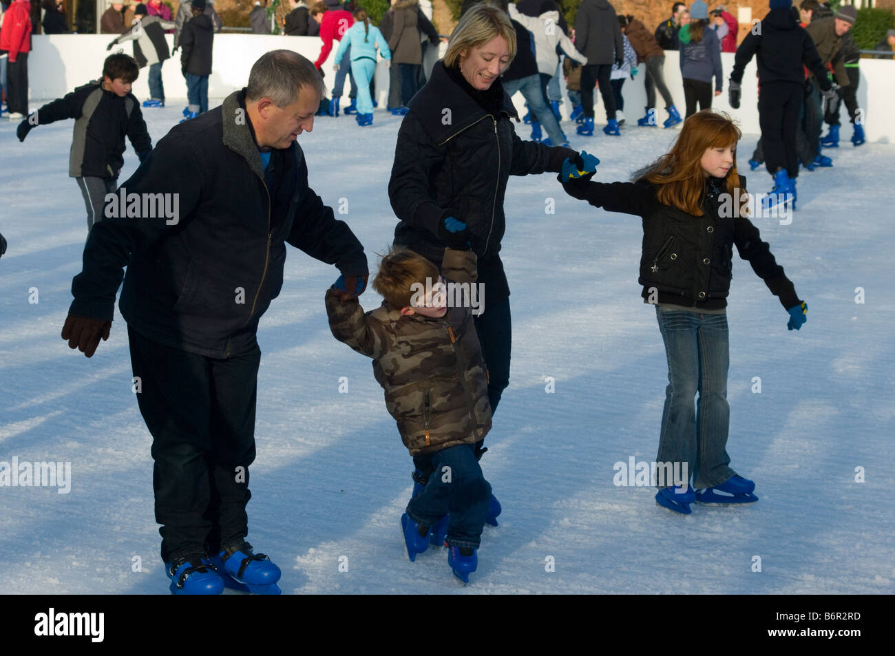 Familia patinaje sobre hielo al aire libre en Hampton Court fuera de pista juntos cogidos de la mano Foto de stock