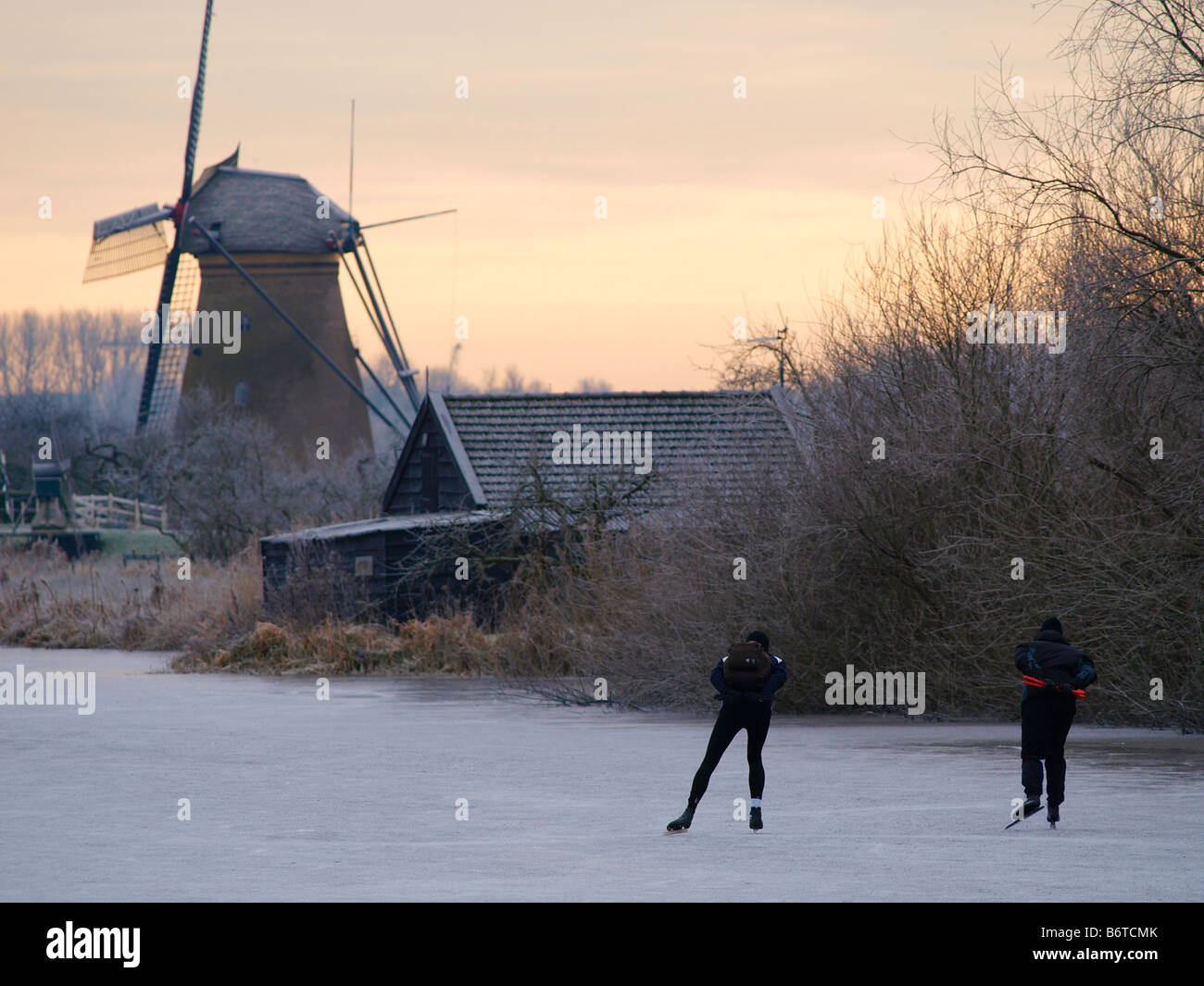 Dos patinadores solitario luchando contra el frío y disfrutar del famoso paisaje de molinos de Kinderdijk Kinderdijk Holanda Foto de stock