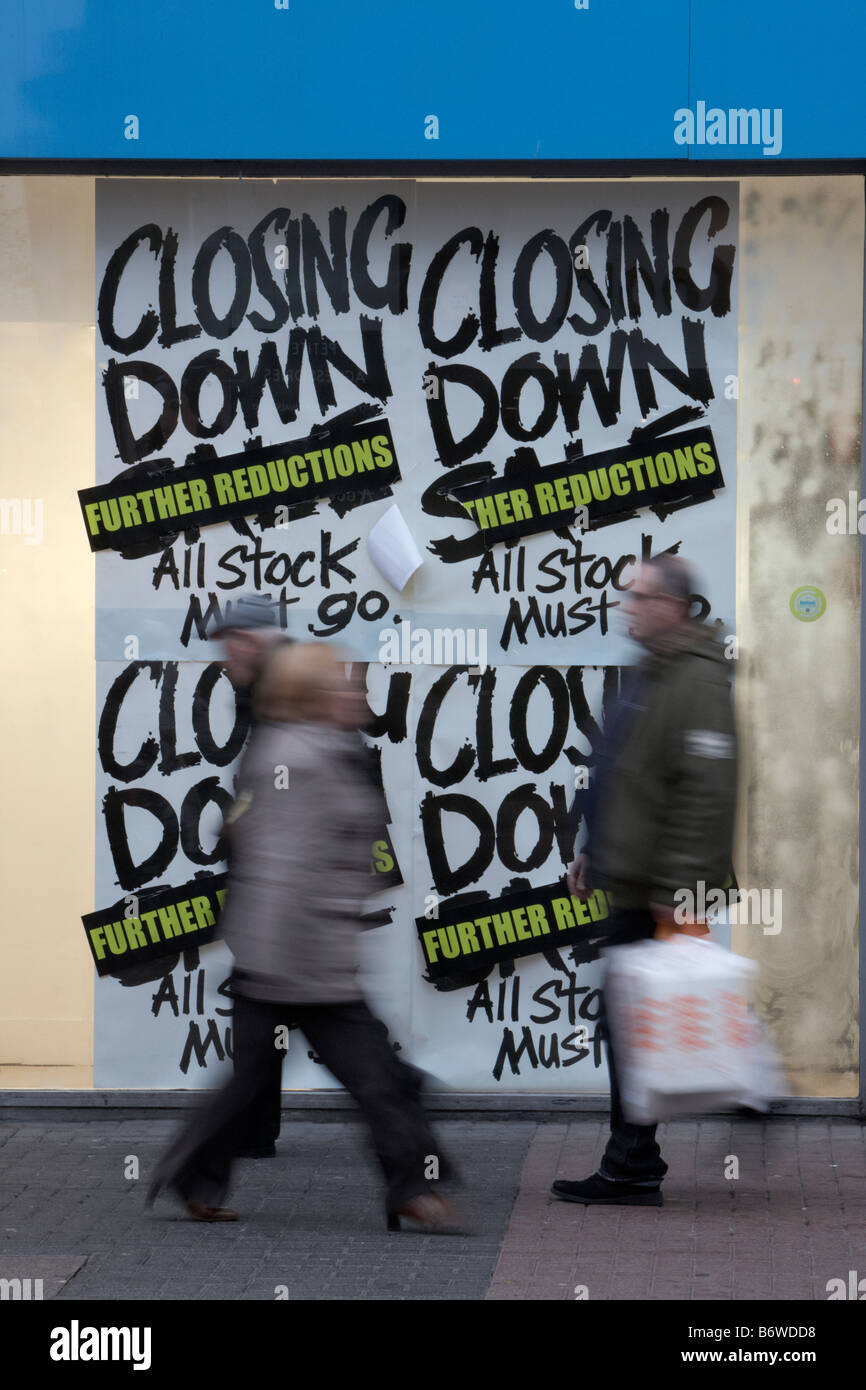 Los compradores pasando cerrando carteles de "Se vende" en un escaparate en el reino unido Foto de stock