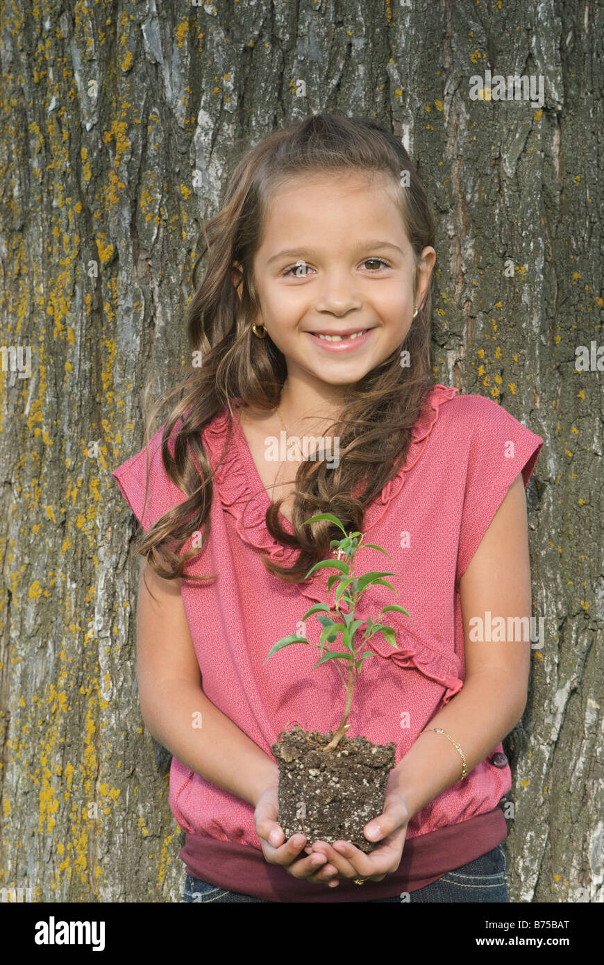 Los siete años de edad, niña celebración seedling junto a árbol, Winnipeg, Canadá Foto de stock