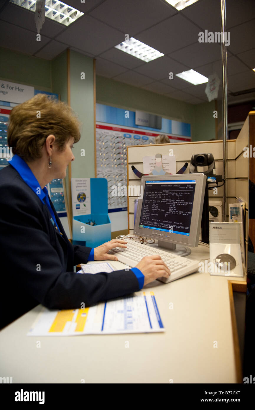 Mujer trabajando en 'olland y Aitchison' D&a entrar en una tienda de ópticas clientes información de prescripción en el equipo UK Foto de stock