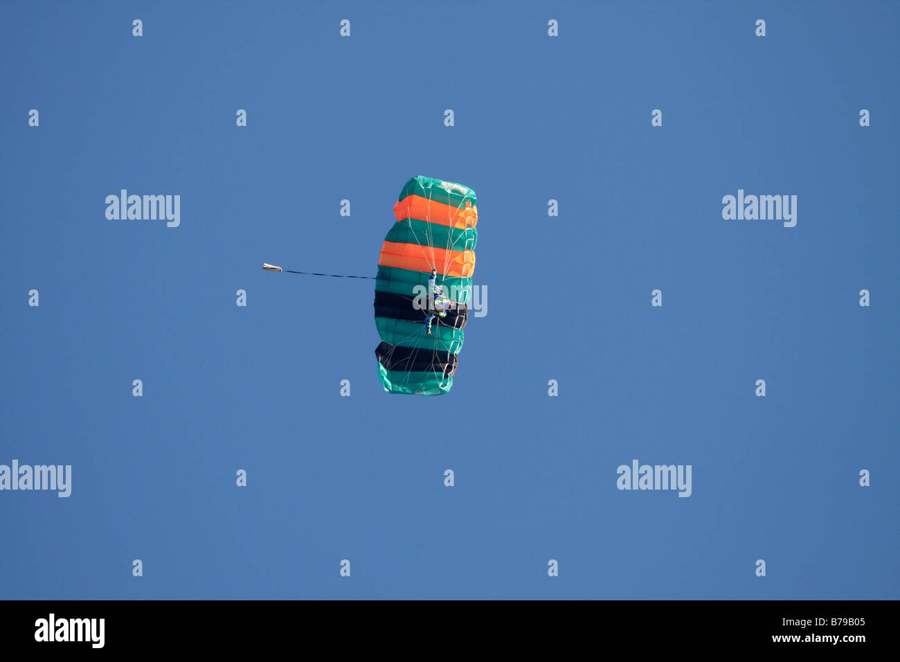 Un paracaidista se cuelga bajo su paracaídas y se desliza a través del cielo azul Foto de stock
